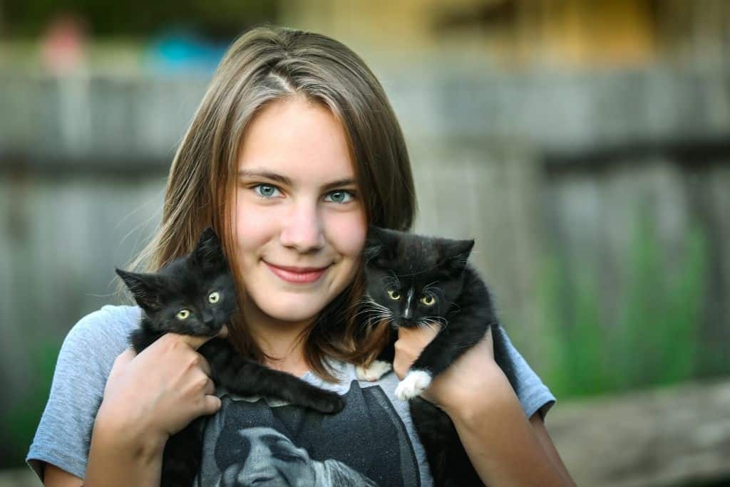 young girl holding two black kittens