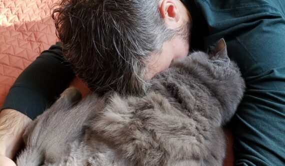 man cuddling grey cat who has only three legs from cancer